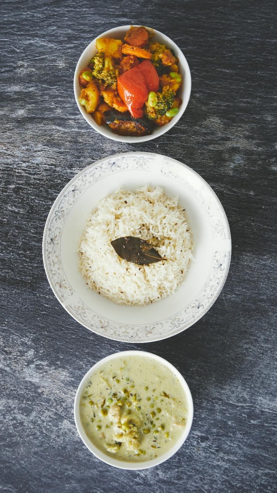 Vegetable curry, cumin rice and a green pea curry served on slate