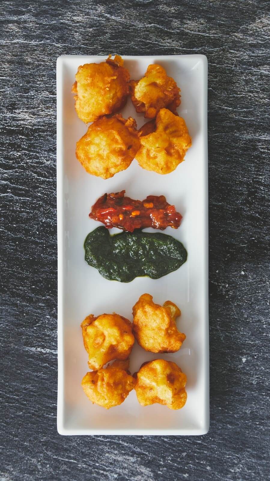 Pakora served on a long white plate with two chutneys