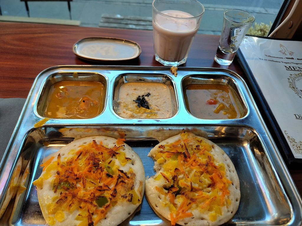 A tray of snacks with three dips and a glass of chai